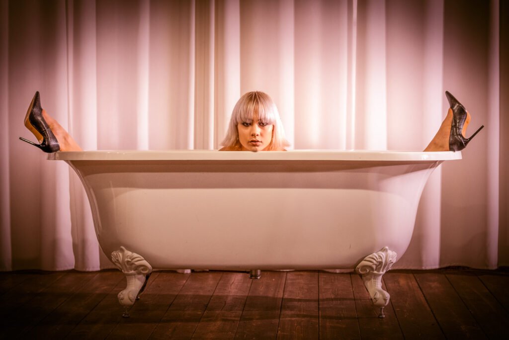 Kreative Foto-Kunst: Frau in einer freistehenden Badewanne vor Vorhängen.