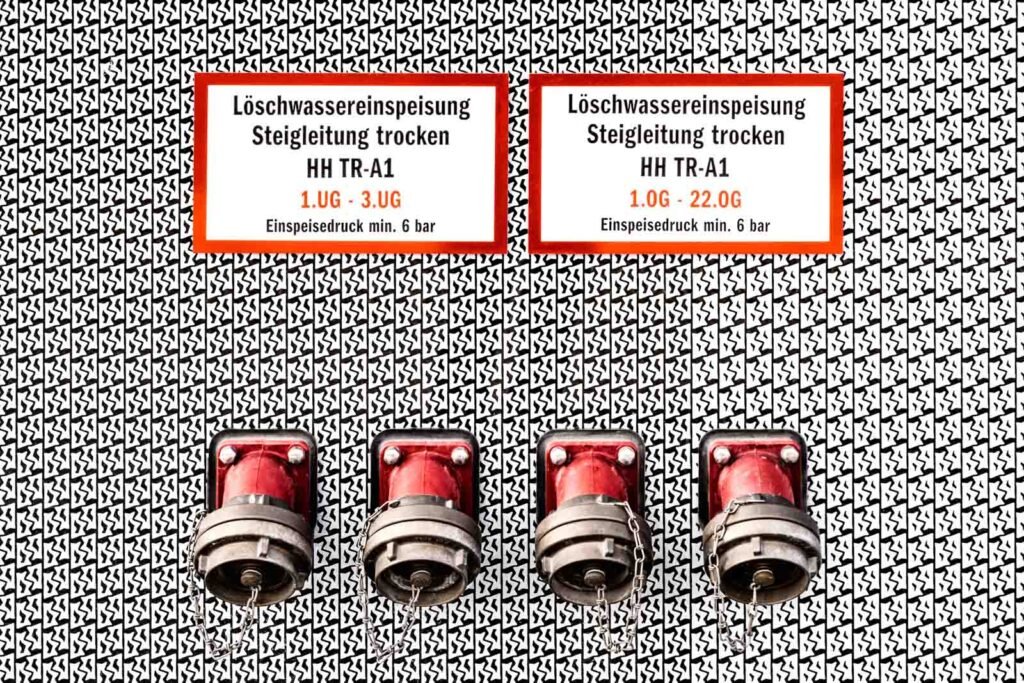 Grafisch gestaltete Nahaufnahme von vier roten Löschwasseranschlüssen vor einem kontrastreichen Musterhintergrund.
