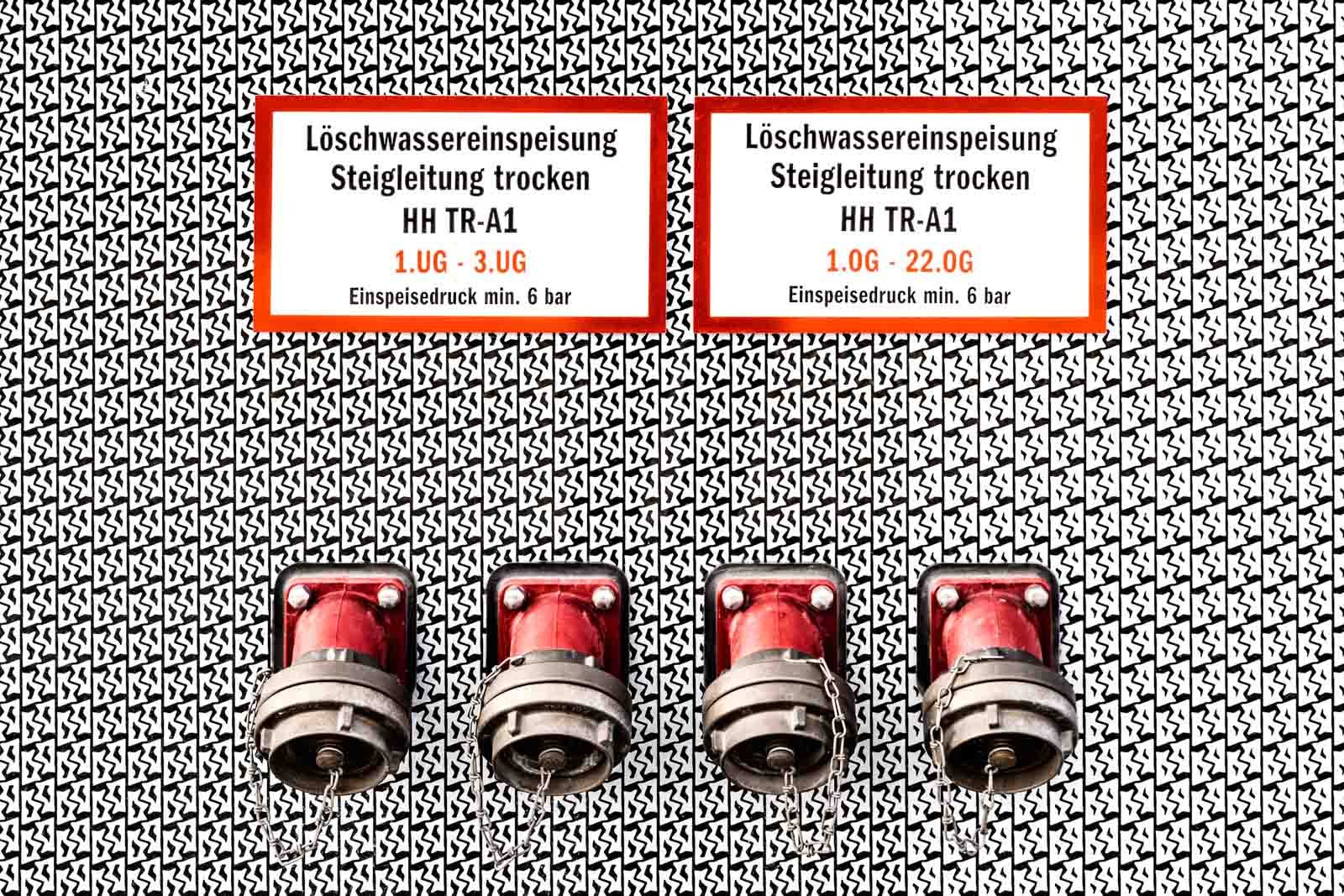 Grafisch gestaltete Nahaufnahme von vier roten Löschwasseranschlüssen vor einem kontrastreichen Musterhintergrund.