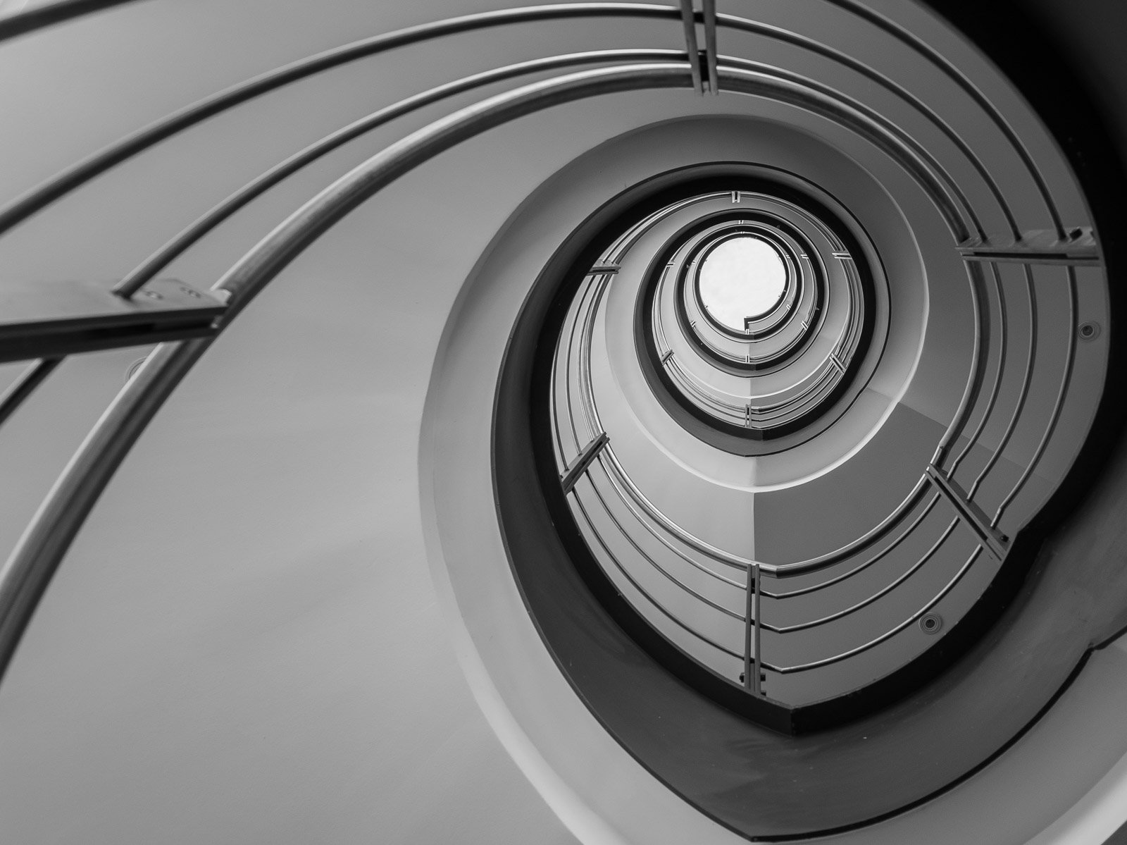 Minimalistische Schwarzweiß-Aufnahme einer Wendeltreppe aus der Froschperspektive.