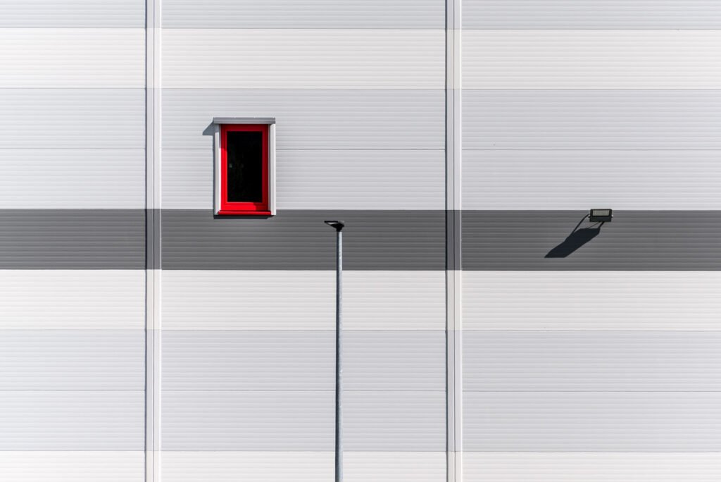 Minimalistische Fassade mit einem markanten roten Fenster und einer Straßenlaterne.