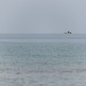 Minimalistische Fotografie Weites Meer mit einem kleinen Boot am Horizont und einer roten Boje im Vordergrund