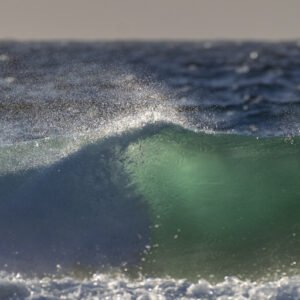 Minimalistische Fotografie „Wellenspiel“: Eine brechende Welle im Gegenlicht als Wandbild im Format 2:1.