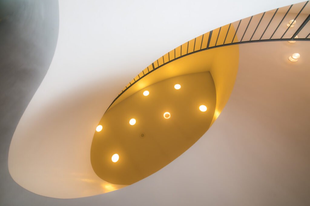 Minimalistische Architekturaufnahme eines Treppenhauses mit geschwungenen Formen und warmen Lichtpunkten.