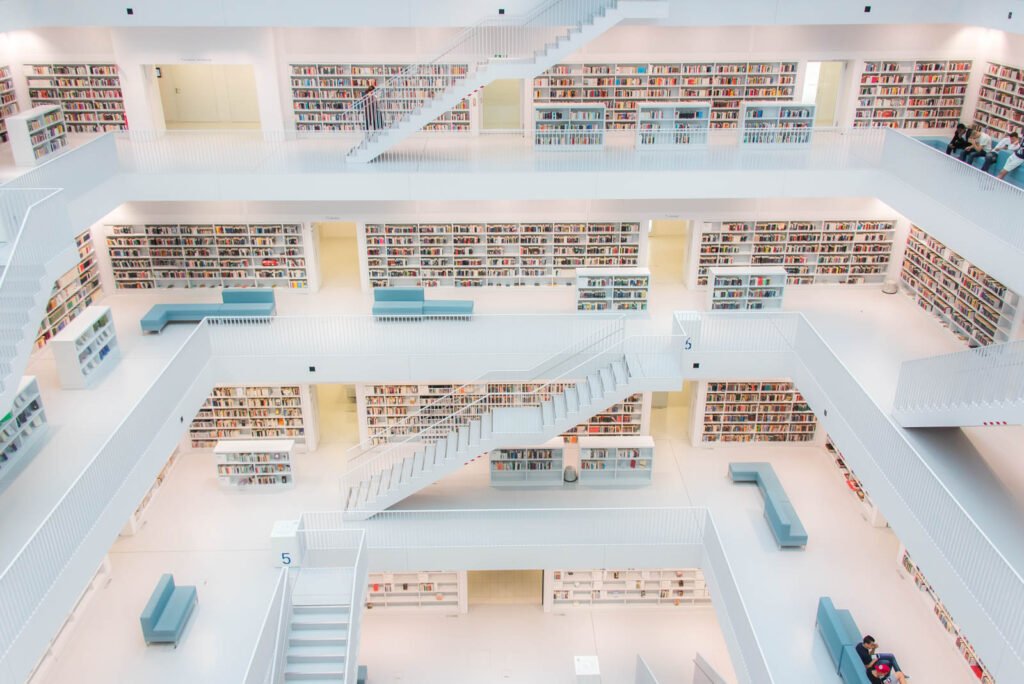 Weitläufige, strahlend weiße Innenarchitektur einer modernen Bibliothek mit symmetrischen Treppenaufgängen und Bücherregalen.