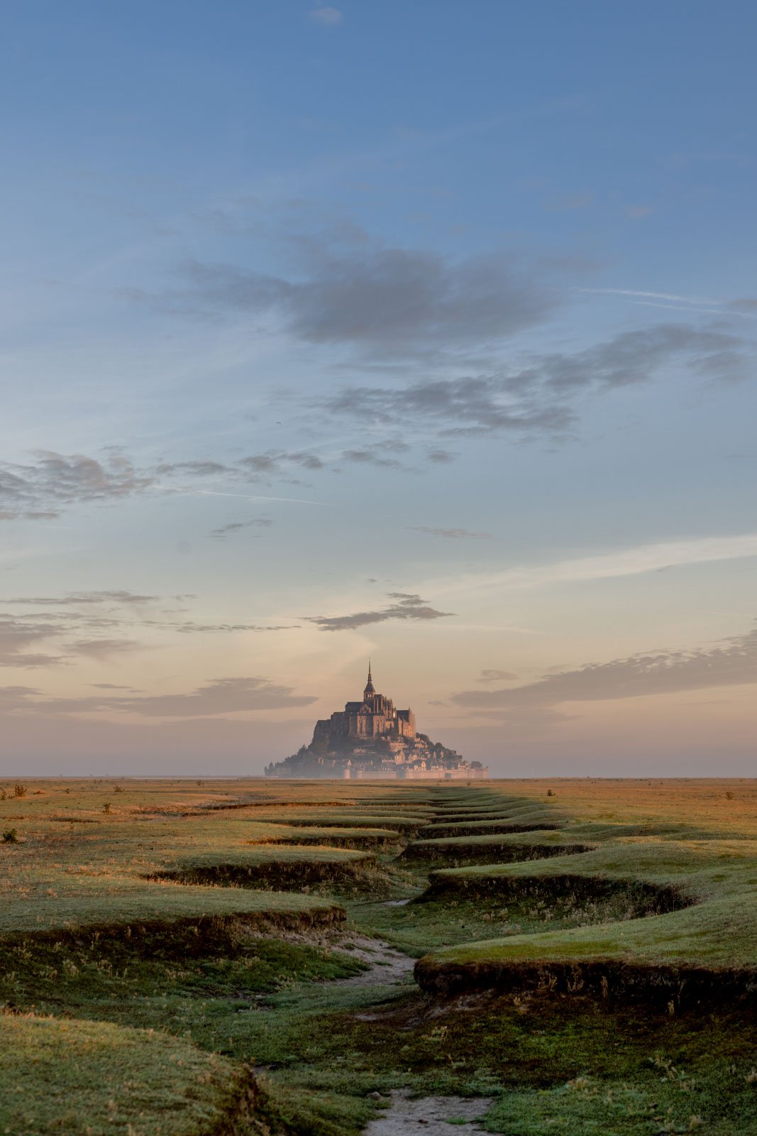 Die Inselburg Mont Saint-Michel in der Normandie bei sanftem Morgenlicht über der weiten Landschaft.