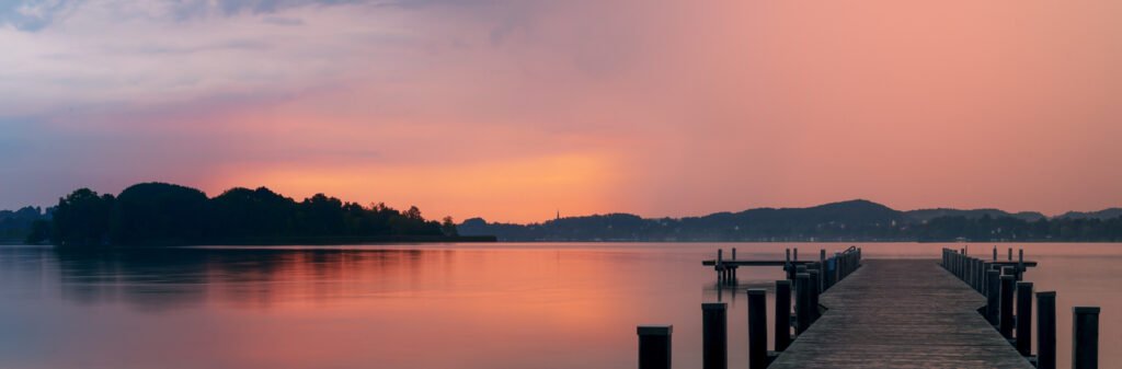 Panorama-Landschaftsfotografie am Wörthsee: Roter Himmel und Steg spiegeln sich im ruhigen Wasser.