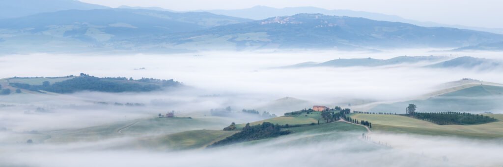 Weites Panorama der toskanischen Landschaft mit tief hängendem Nebel in den Tälern und fernen Bergen.