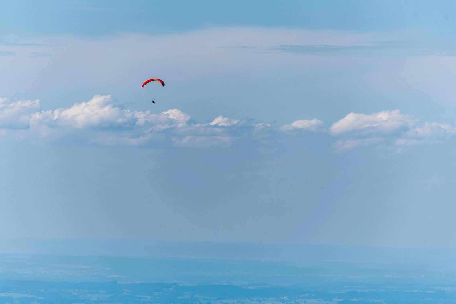 Ein roter Gleitschirmflieger schwebt hoch über den Wolken vor blauem Himmel.