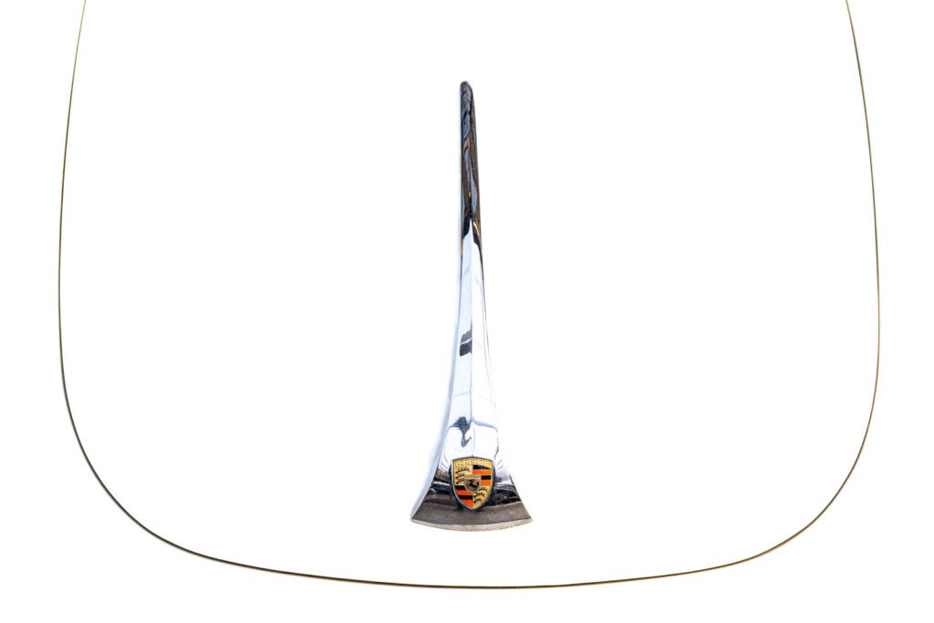 Detailaufnahme der Fronthaube eines Porsche 356 mit verchromter Griffleiste und Porsche-Wappen auf weißem Lack.