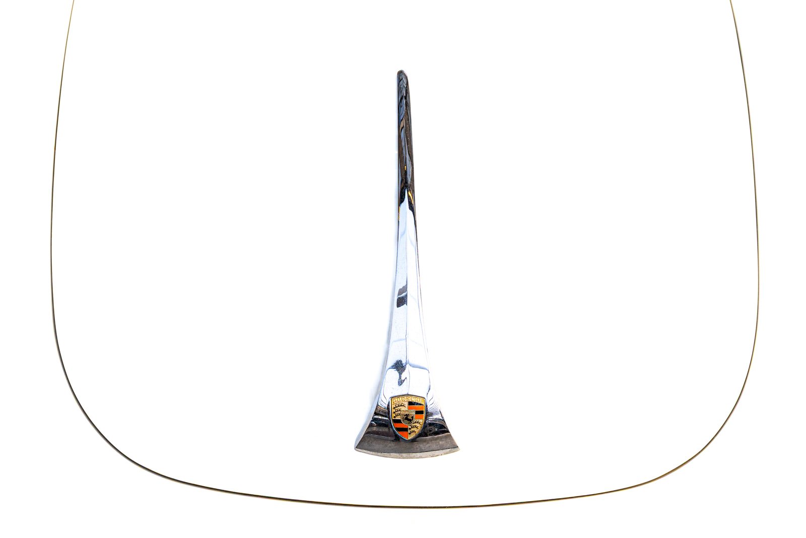 Detailaufnahme der Fronthaube eines Porsche 356 mit verchromter Griffleiste und Porsche-Wappen auf weißem Lack.