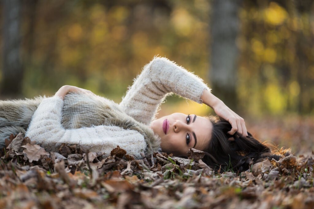 Porträt einer liegenden Frau im herbstlichen Laub mit weichem Bokeh-Hintergrund.
