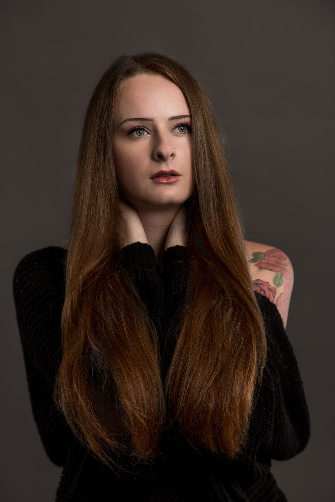 Emotionales Portrait einer jungen Frau mit langen Haaren vor neutralem Hintergrund.