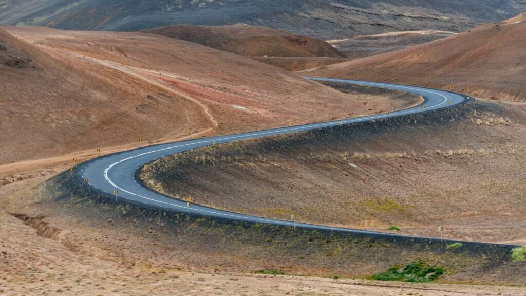 Eine geschwungene S-Kurve einer Landstraße durch eine karge, hügelige Island-Landschaft.