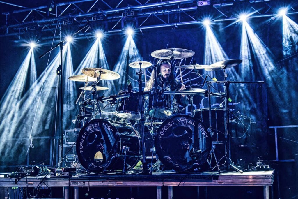 Ein Schlagzeuger spielt ein dynamisches Set auf einer Bühne mit strahlenden Scheinwerfern.