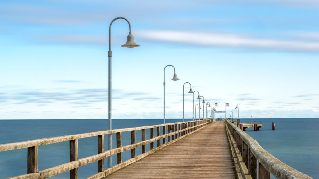 Perspektivische Aufnahme der Seebrücke Göhren auf Rügen mit markanten Laternen vor ruhigem Meer unter blauem Himmel.