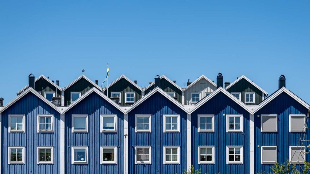 Symmetrische Ansicht blauer skandinavischer Holzhäuser mit Giebeln vor blauem Himmel.