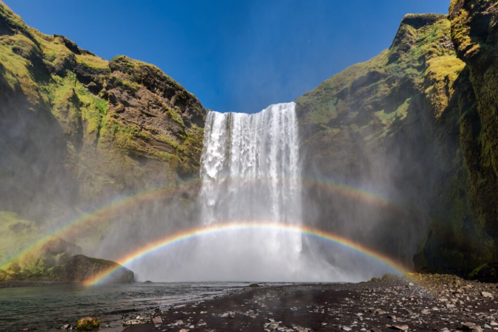 Island Landschaftsfotografie: Der Skogafoss Wasserfall mit doppeltem Regenbogen und viel Gischt.