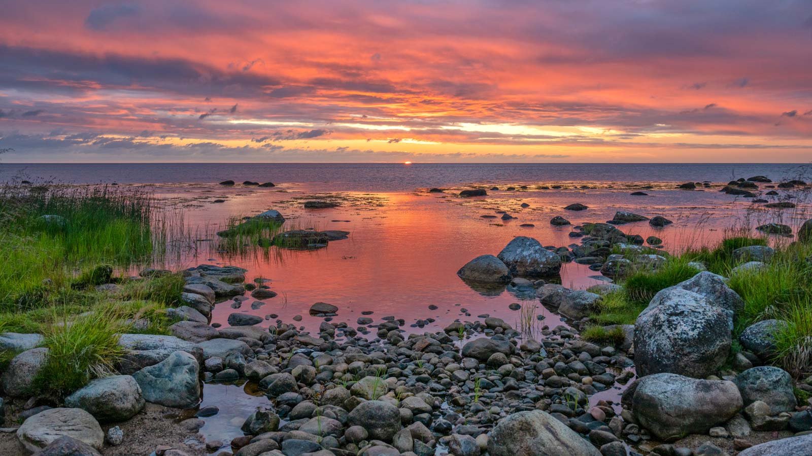 Stimmungsvoller Sonnenaufgang über einer steinigen Küstenlandschaft mit farbenfrohem Wolkenhimmel.