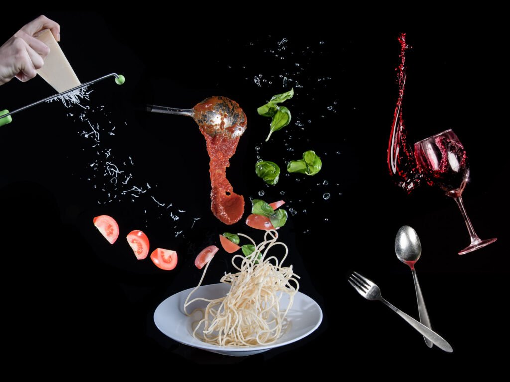 Kreative Food-Fotografie mit fliegenden Spaghetti, Tomaten, Basilikum und Rotwein.