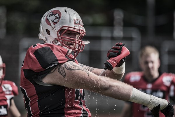 Sportfotografie in Kaufbeuren: Ein American Football Spieler erfrischt sich während einer Spielpause, authentisch eingefangen von Roland Seichter.