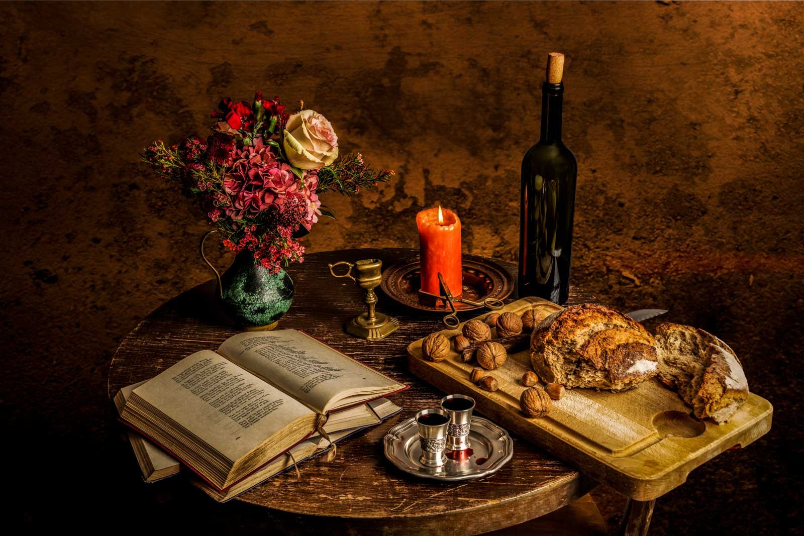 Rustikales Stillleben mit Brot, Walnüssen, Wein und einem offenen Buch bei Kerzenlicht.