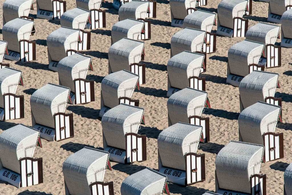 Dicht an dicht stehende, weiß-blau gestreifte Strandkörbe im Sand, die ein rhythmisches Muster bilden.