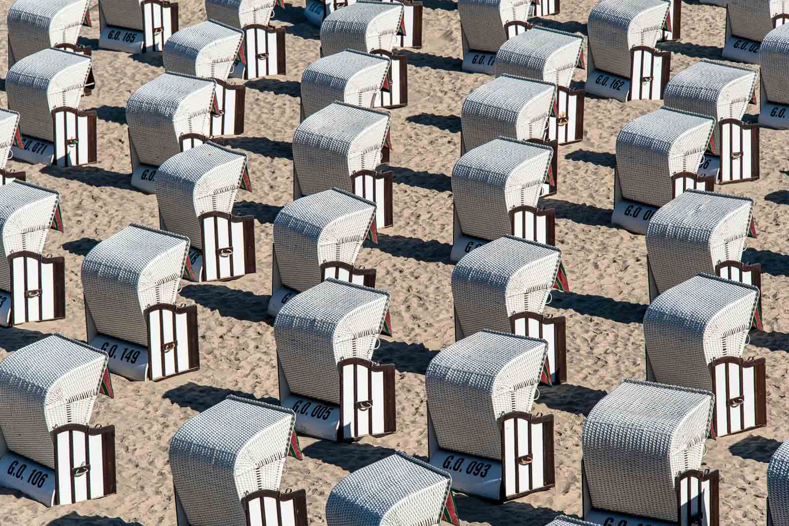 Dicht an dicht stehende, weiß-blau gestreifte Strandkörbe im Sand, die ein rhythmisches Muster bilden.