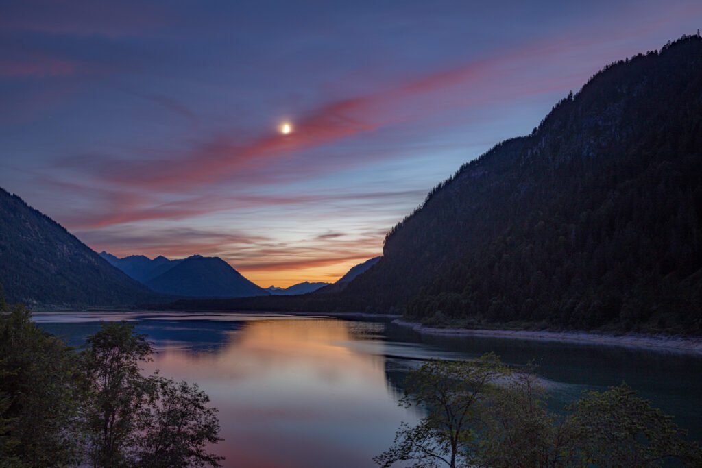 Blaue Stunde am Sylvensteinspeicher: Nachtblauer Himmel, Mond und Bergsilhouette in der Naturfotografie.