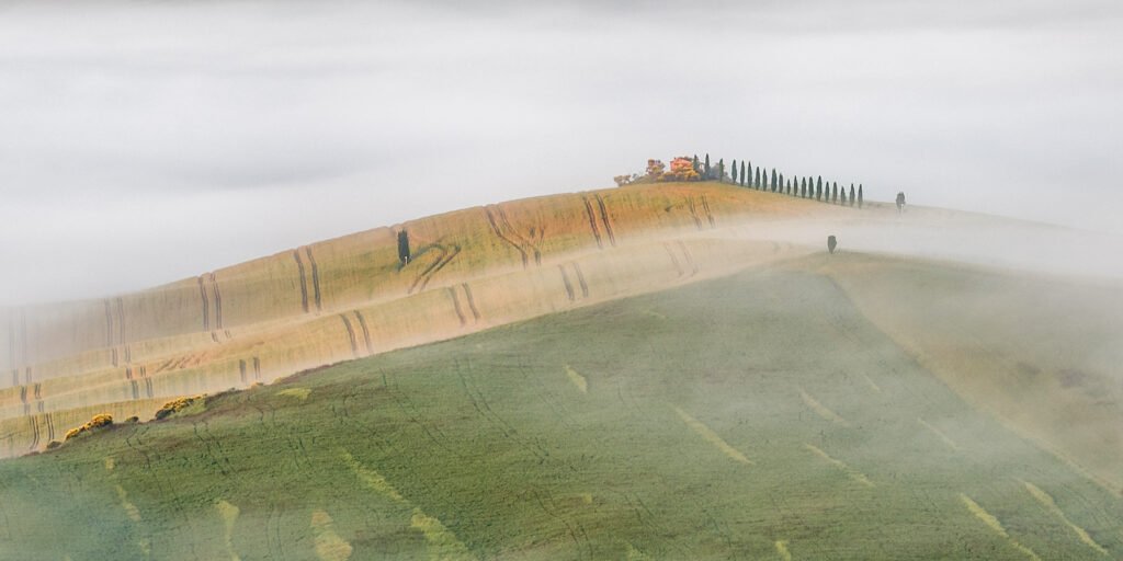 Ein toskanisches Gehöft auf einem Hügelkamm, umhüllt von dichtem Morgennebel und sanftem Licht.