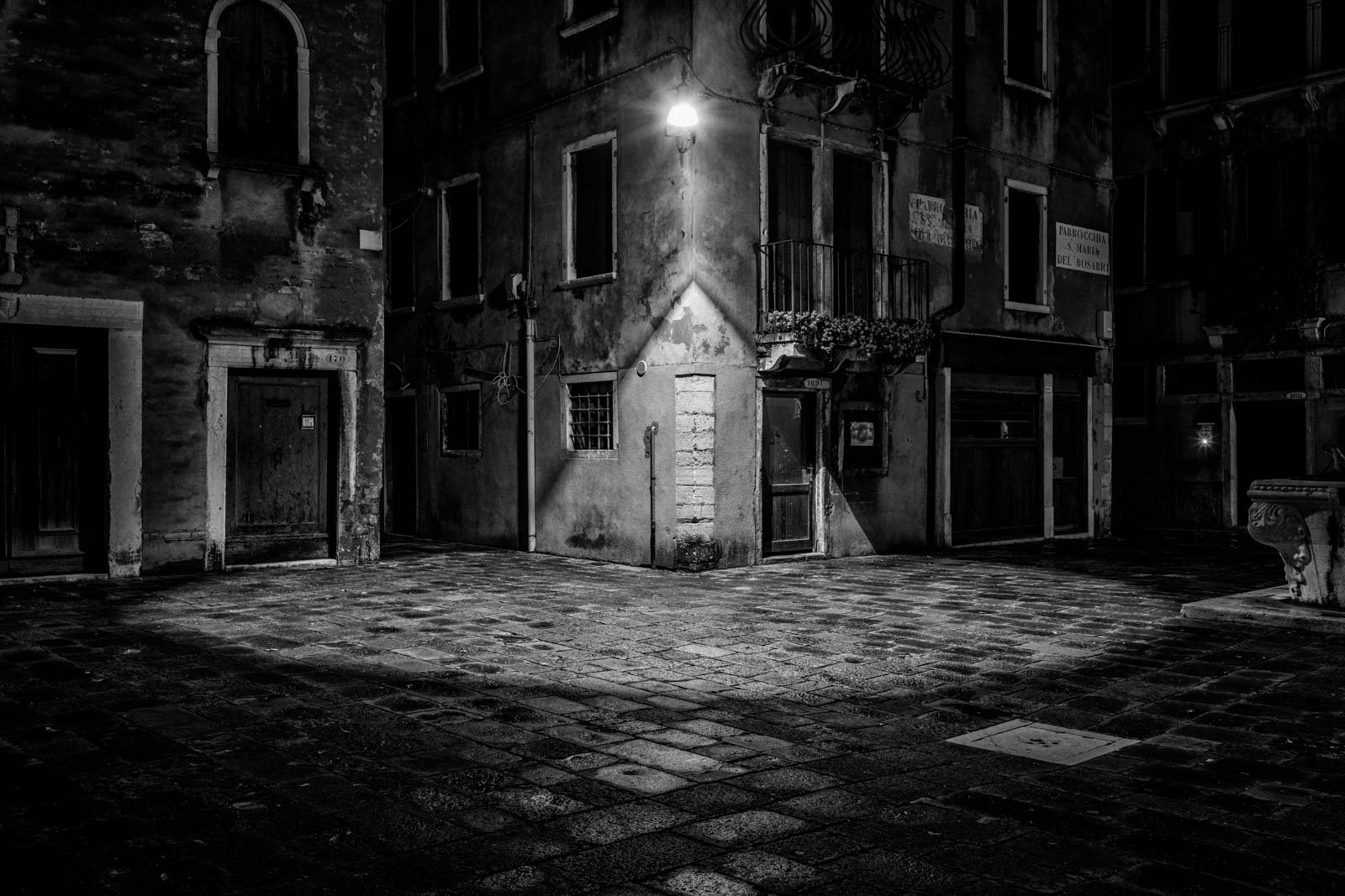 Nächtliche Szene in einer Gasse in Venedig mit einem markanten Lichtkegel einer Straßenlaterne in Schwarz-Weiß.