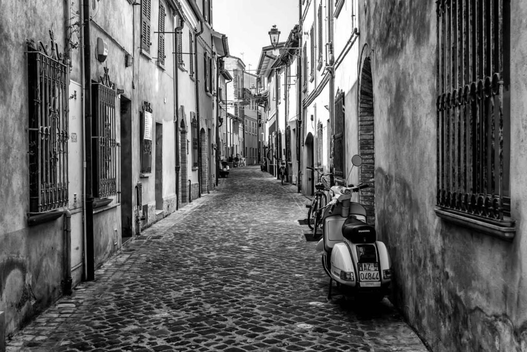 Eine klassische Piaggio Vespa parkt in einer schmalen, gepflasterten italienischen Gasse.