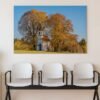 Das Wandbild Herbstliche Kapelle im 3:2 Format als farbenfroher und beruhigender Blickfang an der Wand eines hell gestalteten Wartezimmers.
