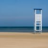 Wandbild "Lifeguard": Ein weißer Rettungsschwimmerturm an einem einsamen Strand vor blauem Meer.