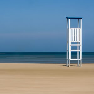 Wandbild "Lifeguard": Ein weißer Rettungsschwimmerturm an einem einsamen Strand vor blauem Meer.