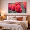 Das Wandbild Rote Tulpen im 3:2 Format als warmer und energetischer Farbakzent an der Wand über einem gemütlich gestalteten Bett im Schlafzimmer.
