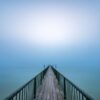 Wandbild "To the Light": Ein langer Steg, der im dichten Nebel über dem Wasser verschwindet.