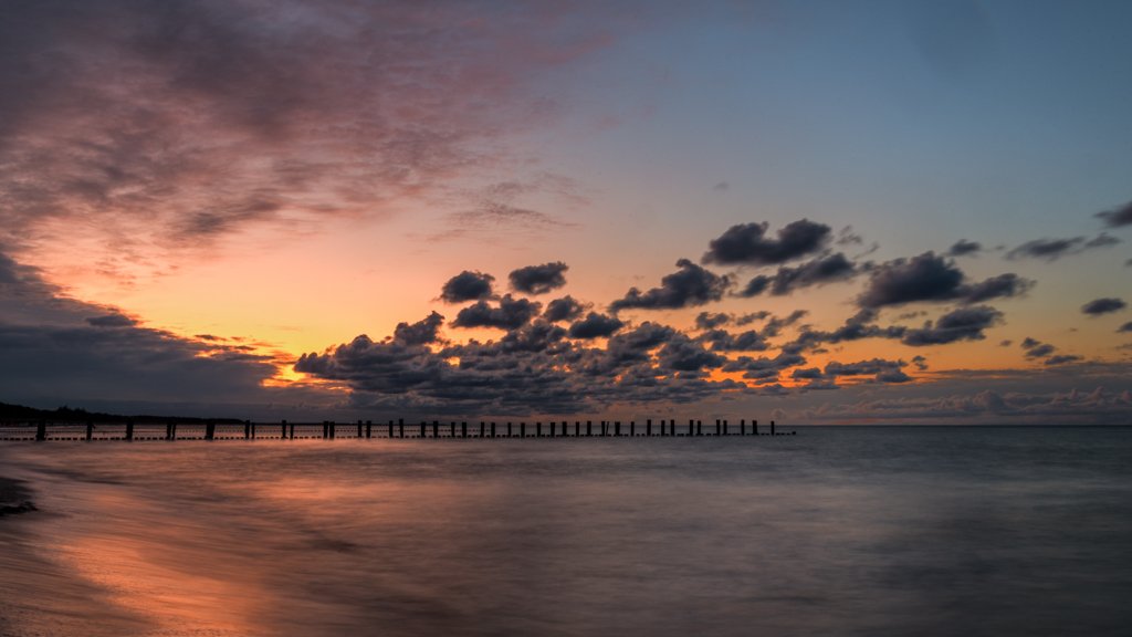 Das Wandbild Abend in Zingst zeigt einen stimmungsvollen Sonnenuntergang an der Ostsee mit Buhnen im Format 16:9.