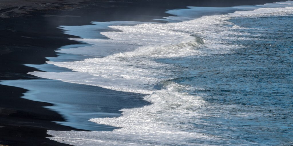 Minimalistisches Praxisbild von Wellen an einem schwarzen Strand – Naturfotografie für Entspannung im Wartezimmer.