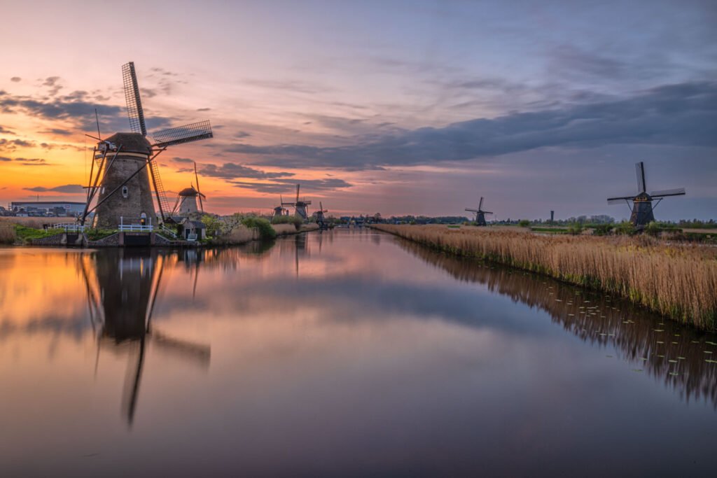 Idyllische Abendstimmung an den Windmühlen von Kinderdijk mit Spiegelungen im ruhigen Kanalwasser bei Sonnenuntergang.