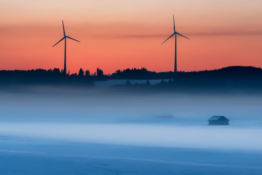 Silhouetten von Windkrafträdern über einer nebligen Winterlandschaft in Bidingen bei Morgenrot.