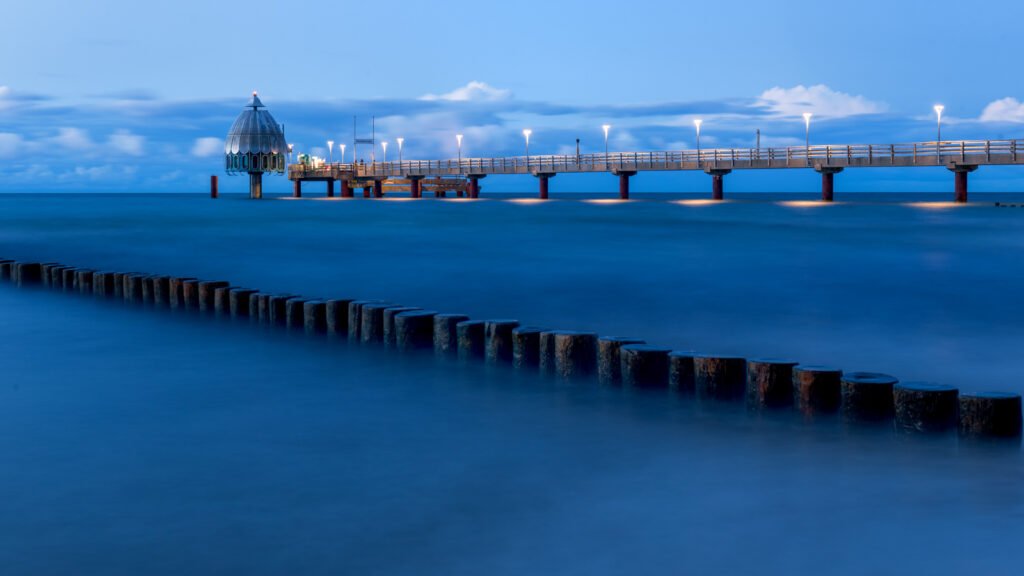 Seebrücke Zingst zur Blauen Stunde: Langzeitbelichtung mit Buhnenreihe und beleuchteter Brücke.